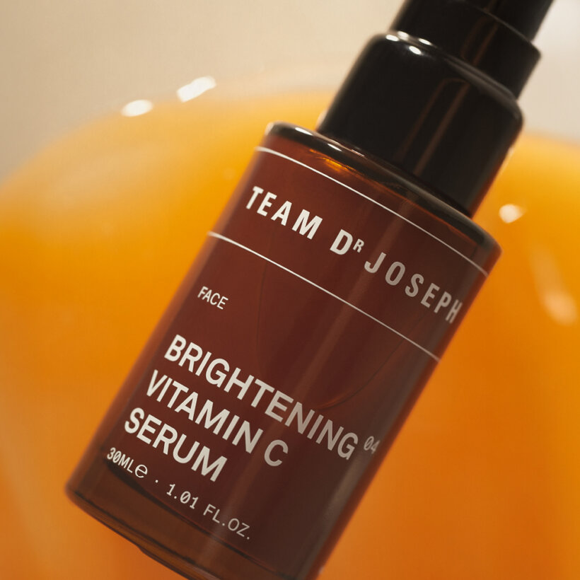 Team Dr Joseph Brightening Vitamin C Serum – Produktmotiv vor orangefarbenem Hintergrund